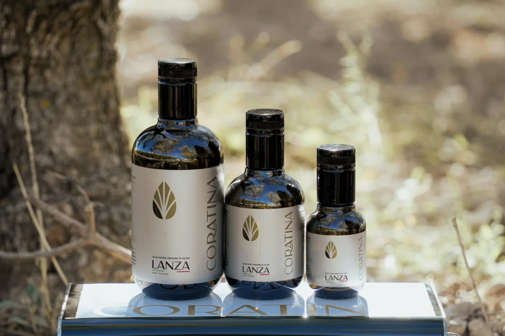 Three bottles of Coratina extra virgin olive oil by Lanza, displayed on branded packaging outdoors in Cerignola, Southern Italy