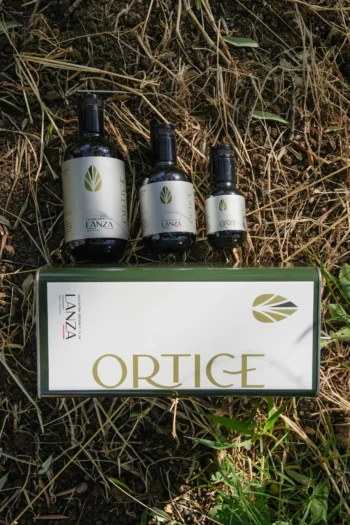 Bottiglie e lattina di olio extravergine Ortice Lanza fotografate su terra e paglia